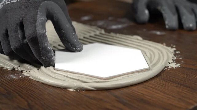 Close-up of a worker's gloved hand carefully placing a white hexagonal tile onto fresh adhesive during a home improvement renovation project