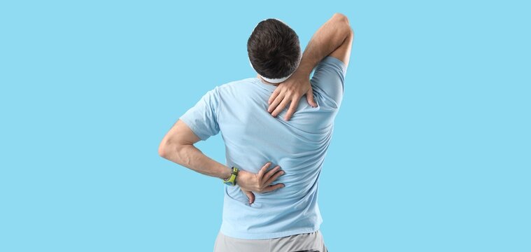 Sporty young man suffering from back pain on blue background