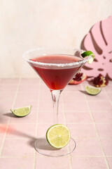 Glass of Cosmopolitan cocktail with lime on pink tile table