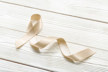Beige ribbon on white wooden background. Uterine cancer awareness concept