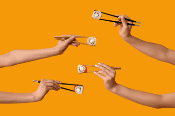 Female hands holding chopsticks with different tasty sushi rolls on yellow background