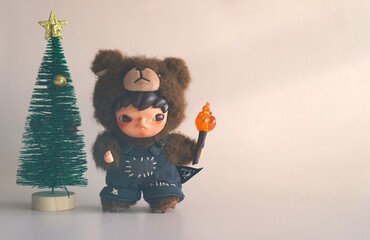 Turkey, October 19, 2025: a miniature Christmas tree with a figurine of a fairy-tale character, a Korean boy dressed as a bear holding a flaming torch, on a gray background
