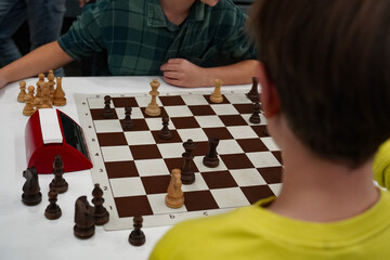  Two players engaged in a serious chess game, concentrating intensely on the board. Chess pieces are strategically placed, while a timer adds pressure to the gameplay