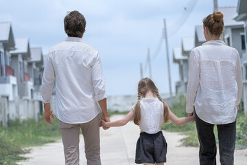 Obraz premium A young family walks hand in hand toward a new housing development. Seen from behind, the parents and their daughter symbolize a journey together towards a new home and a bright future.