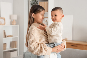 Teenage girl holding her little brother in arms at home