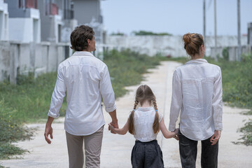 A young family walks hand in hand toward a new housing development. Seen from behind, the parents and their daughter symbolize a journey together towards a new home and a bright future.