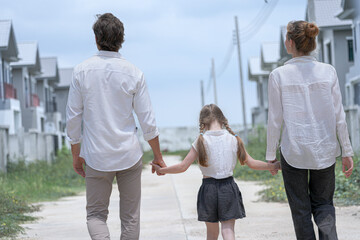 A young family walks hand in hand toward a new housing development. Seen from behind, the parents and their daughter symbolize a journey together towards a new home and a bright future.