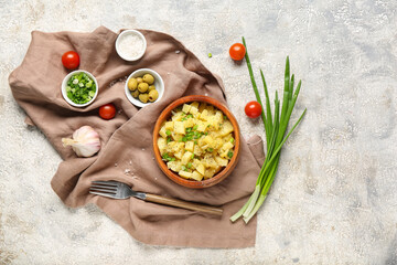 Wooden bowl of tasty potato salad with green onion and ingredients on grey background