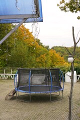 Outdoor trampoline set in a backyard during autumn, surrounded by vibrant orange and green foliage. The patio area is paved, and decorative lights hang above, enhancing the cozy atmosphere.