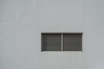 Rectangular metal ventilation grille on gray textured wall, minimalist industrial exterior detail.
