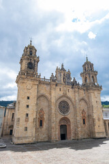 Fototapeta premium Historic stone cathedral of Mondonedo, Galicia, Spain, with ornate towers and a large rose window under dramatic clouds in a quiet plaza,