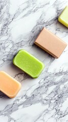 A top-down view of three colorful bars of soap and one wrapped soap bar arranged diagonally on a marble background.