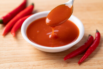 Sriracha sauce in a bowl with spoon on wooden background, Chili sauce