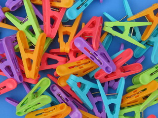 Closeup of multicolored plastic clothes peg on blue background. Multicolored plastic clothes pegs scattered on blue background.