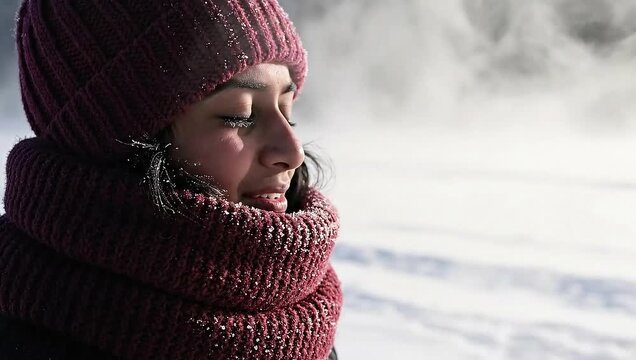 A young woman in a red hat and scarf exhales visible breath in cold winter air, creating a cloud of vapor.