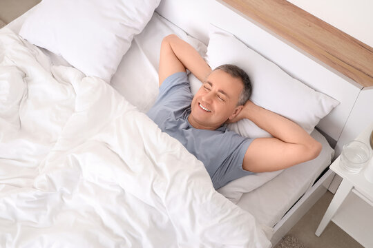 Mature man lying under blanket in bedroom, top view