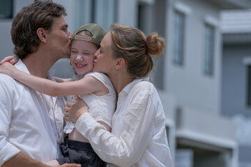 Obraz premium A hopeful young family looks towards their future outside a new modern home. The father holds their daughter, who points excitedly, as the mother smiles, dreaming of their life together.
