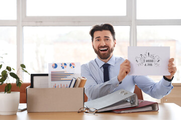 Naklejka premium Fired young man holding paper with text I NEED A JOB at table in office