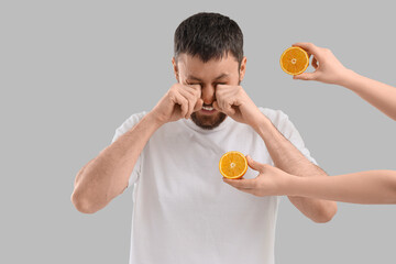 Sick young man and female hands with orange on light background. Food Allergy Awareness Month