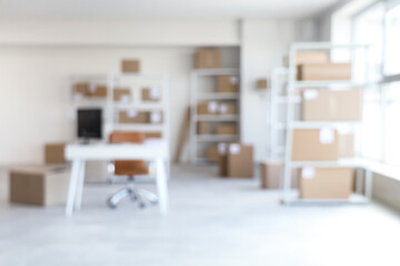 Blurred view of warehouse with workplace, shelf units and cardboard boxes
