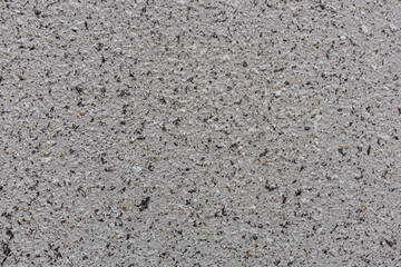 Detailed close-up view of grey concrete surface, showing speckled texture with small dark pebbles and granular grains which give it rough sandpaper-like appearance.