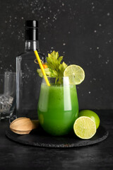 Glass of green bloody mary cocktail garnished with lime, physalis berry and cucumber slice on black background