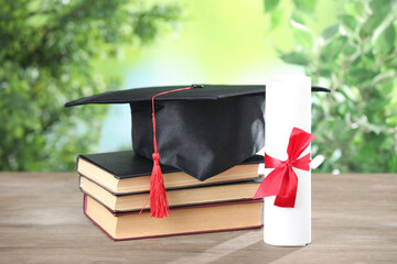 Graduation cap, diploma and books on wooden table against blurred background, closeup