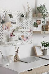 Workplace with blossoming branches and pegboard on light wall in office