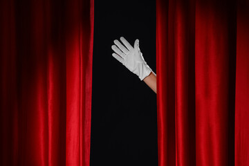 Female hand in glove behind red curtains on black background