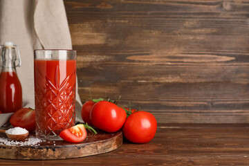 Glass of fresh tomato juice and spoon with salt on wooden background