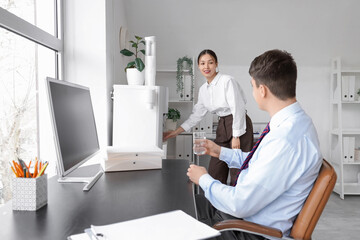 Obraz premium Young Asian businesswoman pouring water from cooler in office