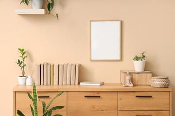 Chest of drawers with houseplants and books near beige wall in interior of room