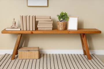 Photo frame, houseplant and books on bench near beige wall in room, closeup
