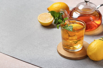 Glass and teapot of lemon ice tea with mint on beige background, closeup
