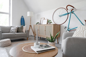 Interior of light living room with bicycle, sofa and armchair