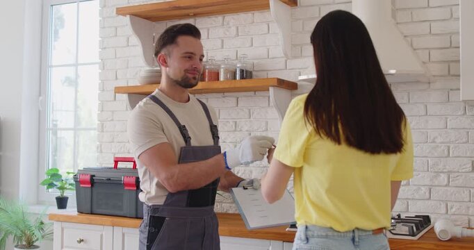 Positive workman and female client shaking hands in home kitchen during repair or maintenance, offering service assistance, completing renovation, ensuring professional care and support.