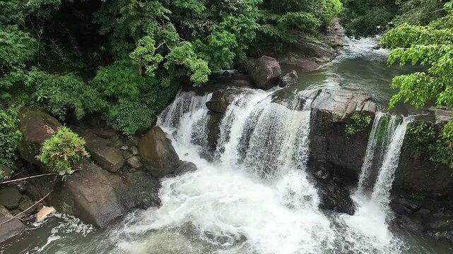 Top view of a wide waterfall originating from a river in the middle of a tropical forest with a zoom out or dolly out camera movement.