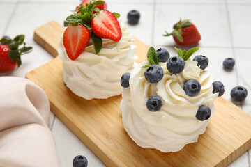 Wooden board with sweet Pavlova cakes with fresh berries and mint on white tile background, closeup