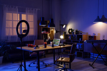 Interior of dark studio with podcaster's workplace, shelf units and glowing lamps