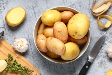 Bowl of raw baby potatoes with garlic and thyme on grey background
