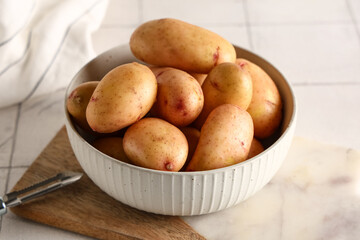 Bowl with raw baby potatoes on white tile background, closeup