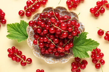 Bowl with fresh red currants and leaves on yellow background