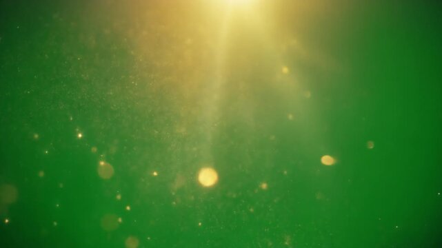 A radiant golden sunbeam illuminates sparkling dust particles and soft bokeh against a vibrant green background.