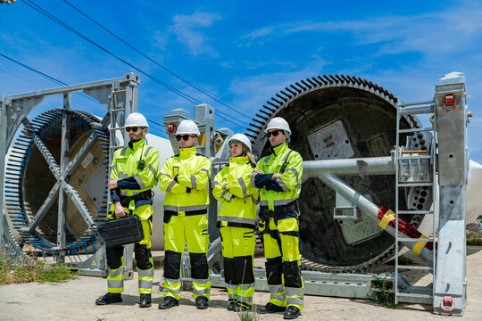 engineers in hard hats and high-visibility jackets inspect a massive piece of industrial equipment on a construction site, collaborating to ensure safety and proper assembly.