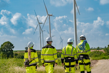  group of engineers in high visibility gear stands at a wind farm, observing several wind turbines. The image highlights teamwork, renewable energy, and the scope of wind power projects.