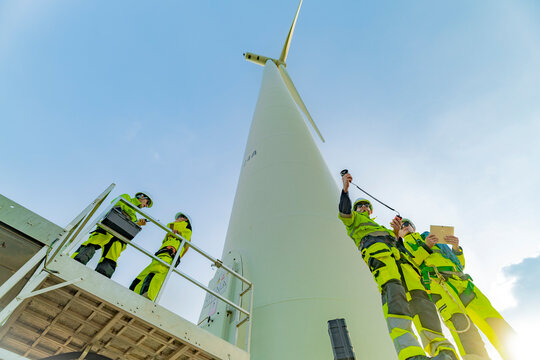A team of engineers inspects and maintains a large wind turbine at a renewable energy wind farm. Green technology and sustainable practices are at the forefront of renewable energy development. - Powered by Adobe