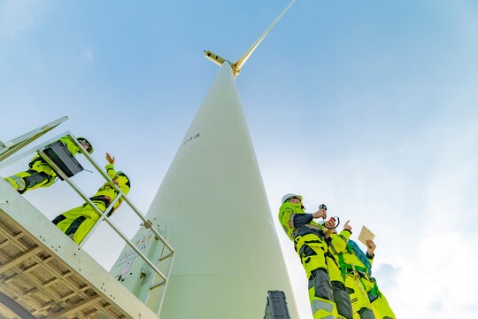 A team of engineers inspects and maintains a large wind turbine at a renewable energy wind farm. Green technology and sustainable practices are at the forefront of renewable energy development.