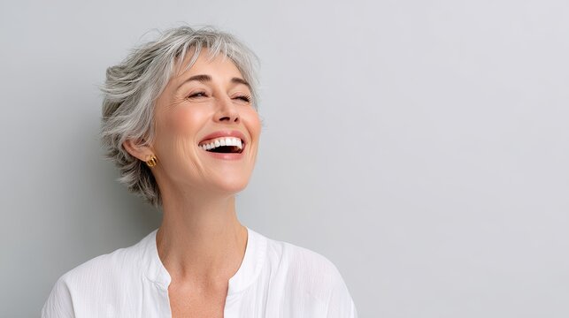 Joyful middle-aged woman with short gray hair beams with happiness against a soft gray background in this uplifting portrait photography image.