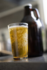 Bubbly glass of beer next to glass growler container, beer in a sunny kitchen, home brew