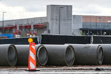 Concrete drainage pipes staged at a commercial construction site with barricades and a large retail...